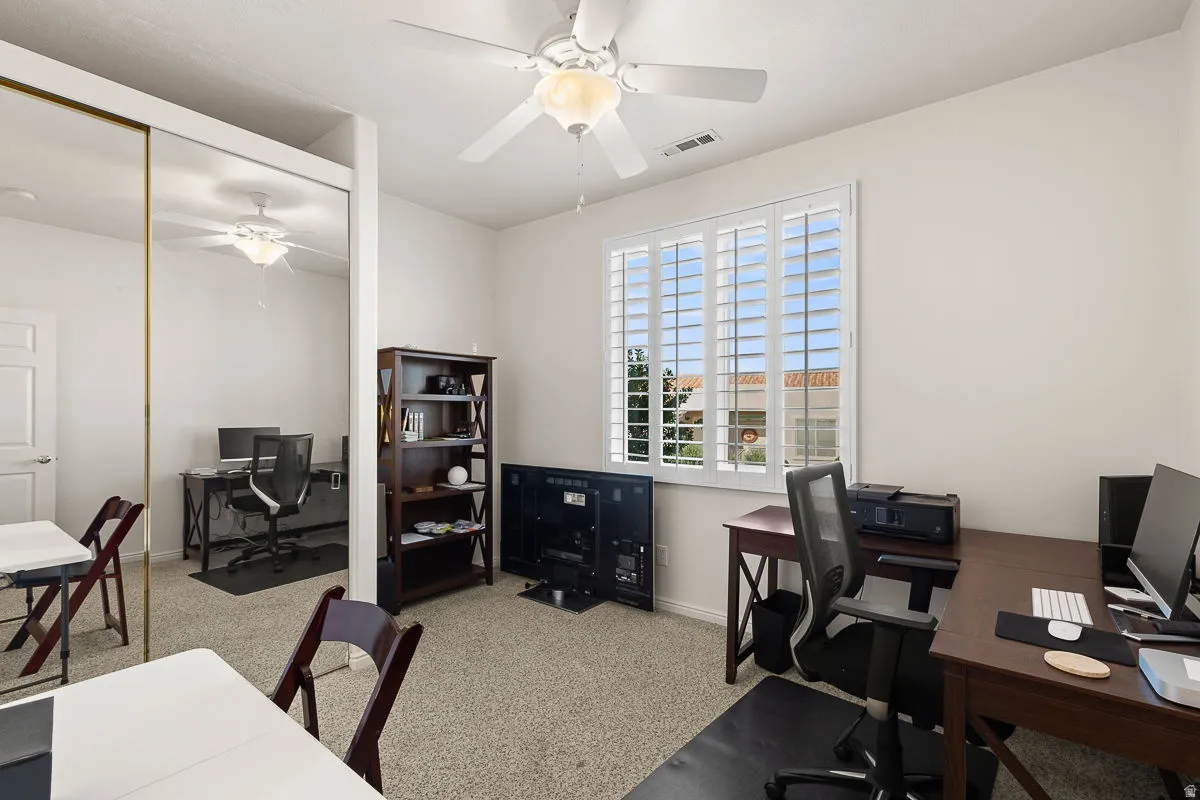 Spacious room featuring neutral carpet flooring, a ceiling fan with light fixture, and a window with white plantation shutters