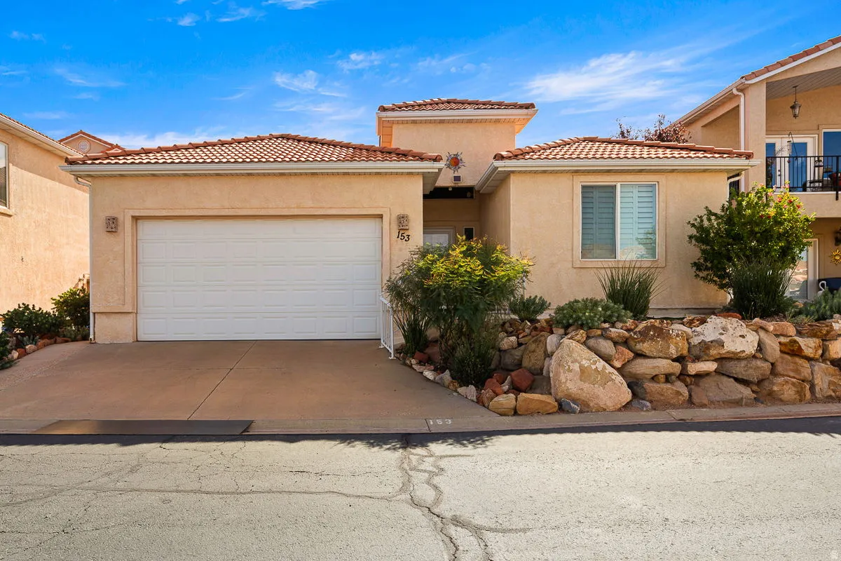 Southwestern-style stucco exterior featuring a two-car garage, concrete driveway, and a terra cotta tile roof