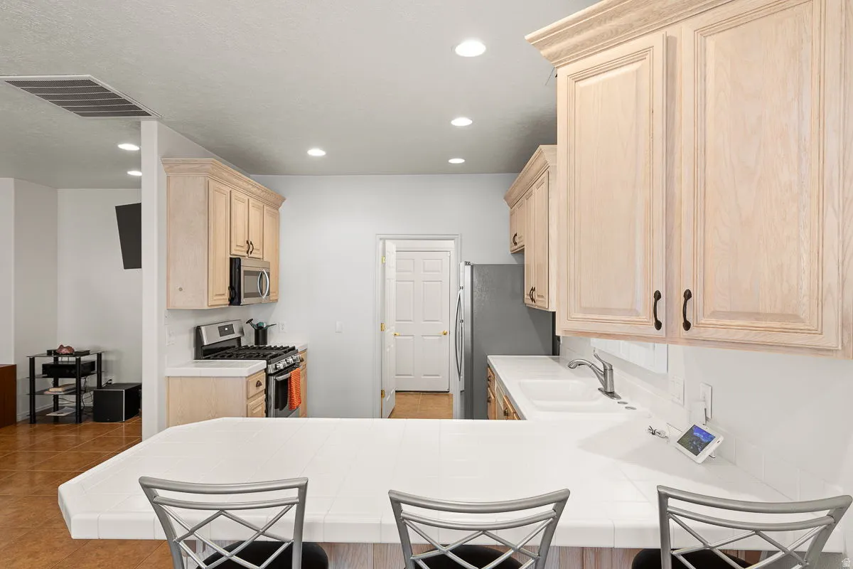 Kitchen featuring a breakfast bar with white tile countertop, recessed lighting, wood-finish cabinetry, and stainless steel appliances