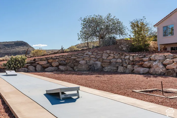 Backyard featuring a paved recreational court, natural stone retaining wall, desert landscaping, and prominent mountain backdrop