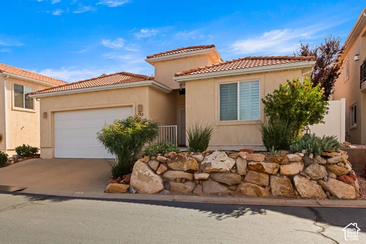 Stucco exterior with a tiled roof, integrated garage, and a decorative rock retaining wall
