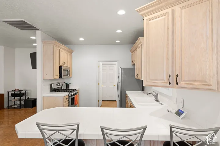 Kitchen featuring a breakfast bar with white tile countertop, recessed lighting, wood-finish cabinetry, and stainless steel appliances