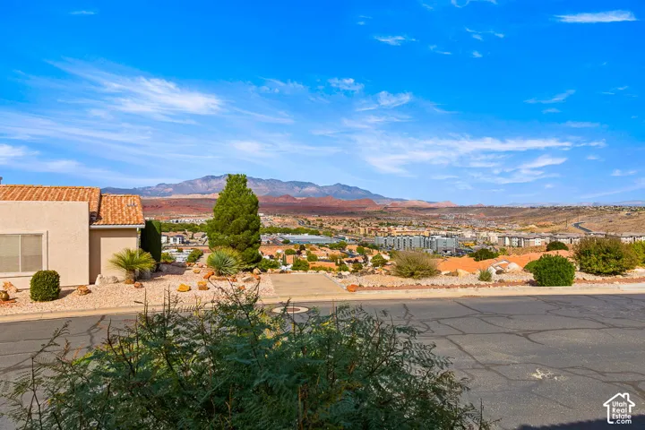 Tan stucco residence featuring a terra cotta tile roof and a xeriscaped front yard with decorative rocks, mature shrubs, and an established evergreen tree