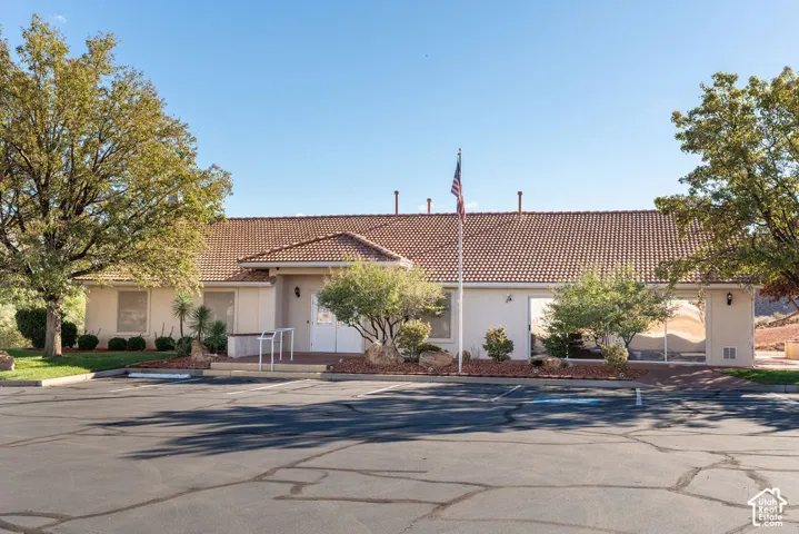 Exterior facade featuring a terracotta-style tile roof, stucco finish, covered entryway, and asphalt-paved parking area