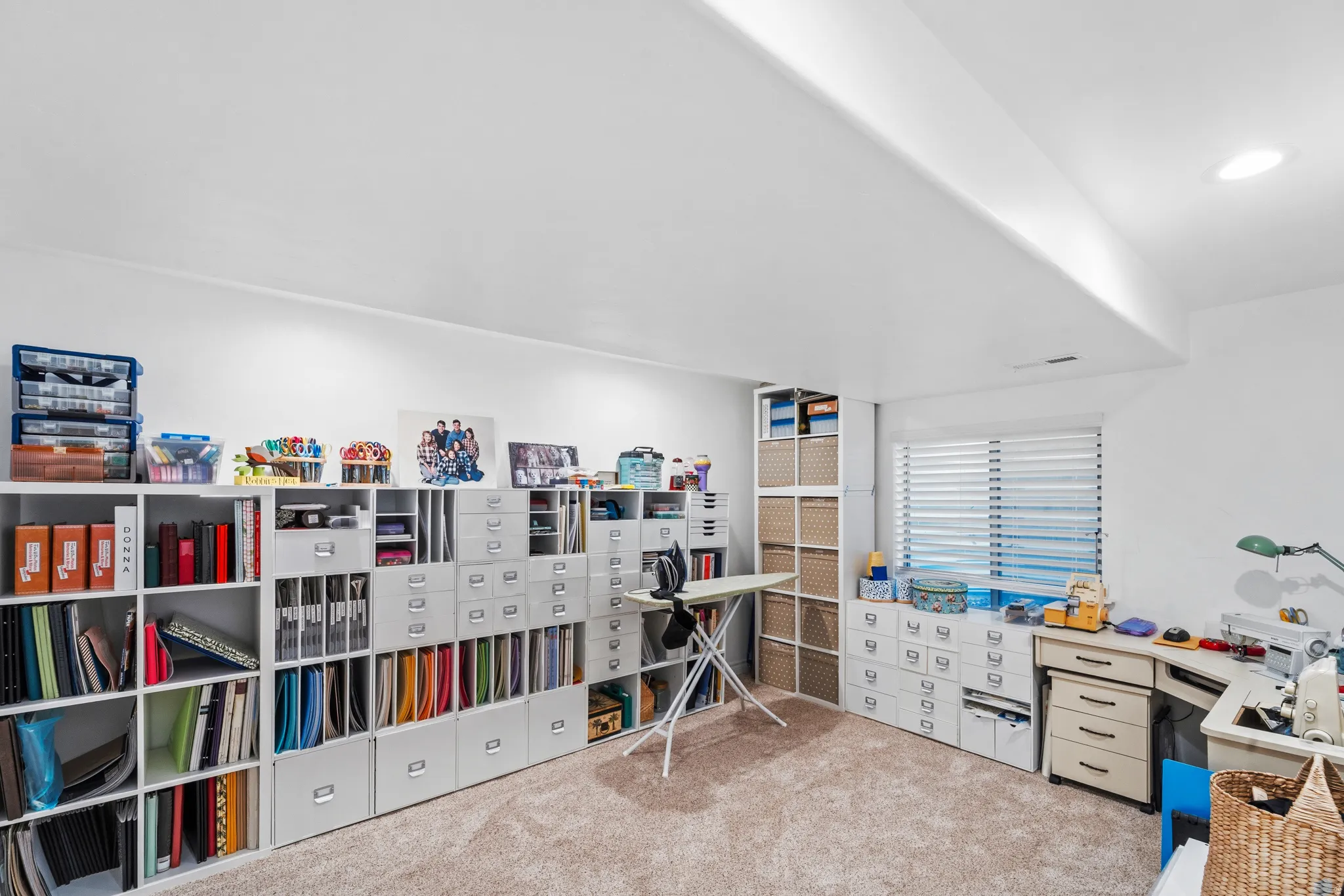 Versatile room featuring extensive built-in modular shelving, neutral carpeting, recessed lighting, and a window with horizontal blinds