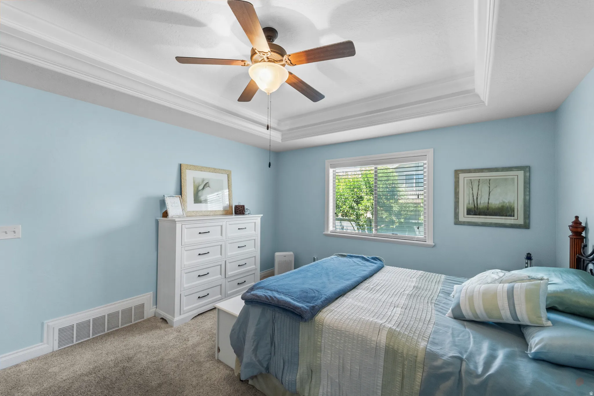 Bedroom featuring a tray ceiling with crown molding, a ceiling fan with light fixture, a window with blinds, and carpeted flooring