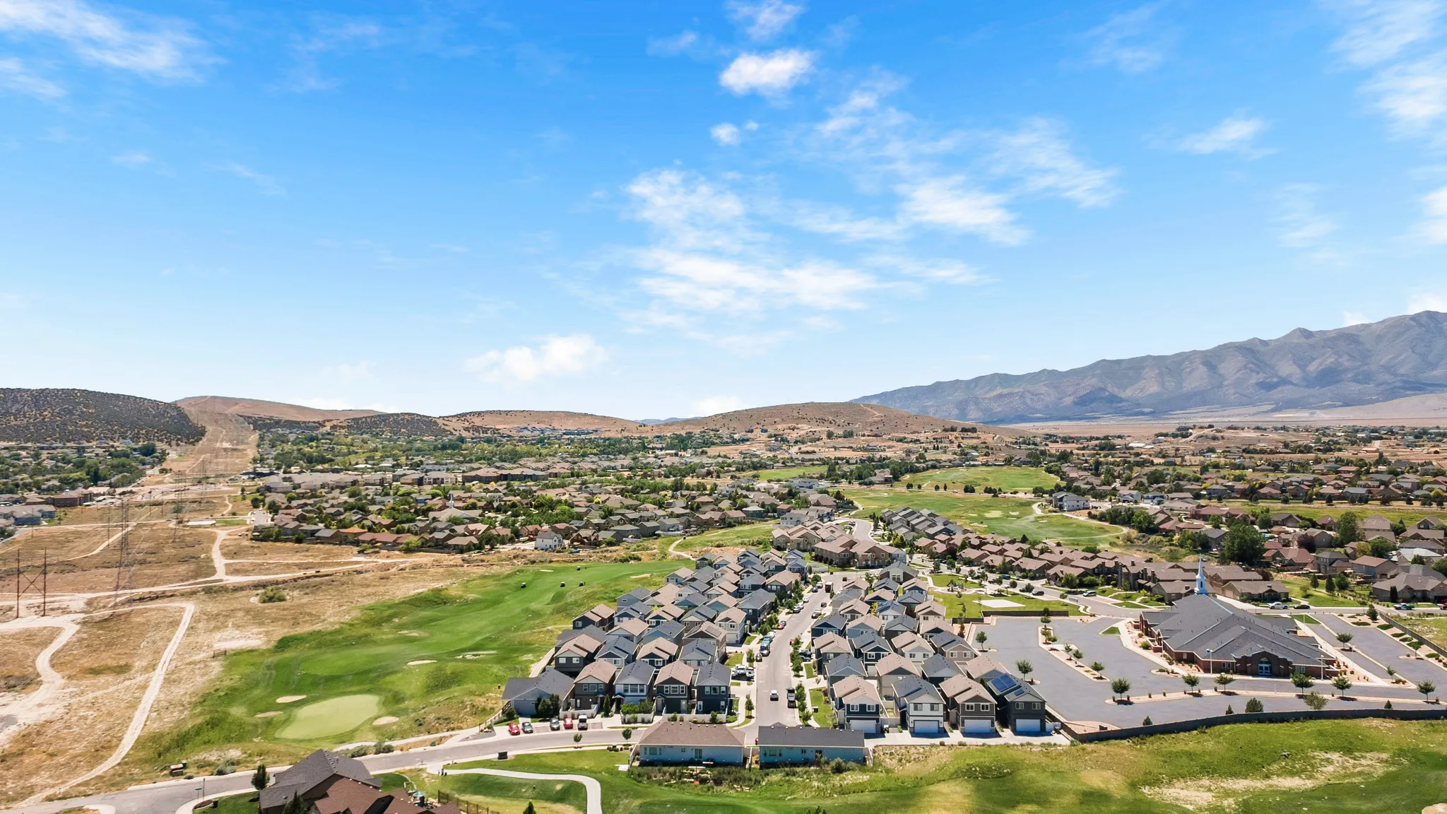 Residential development with mountain backdrop, golf course greens, and a community building