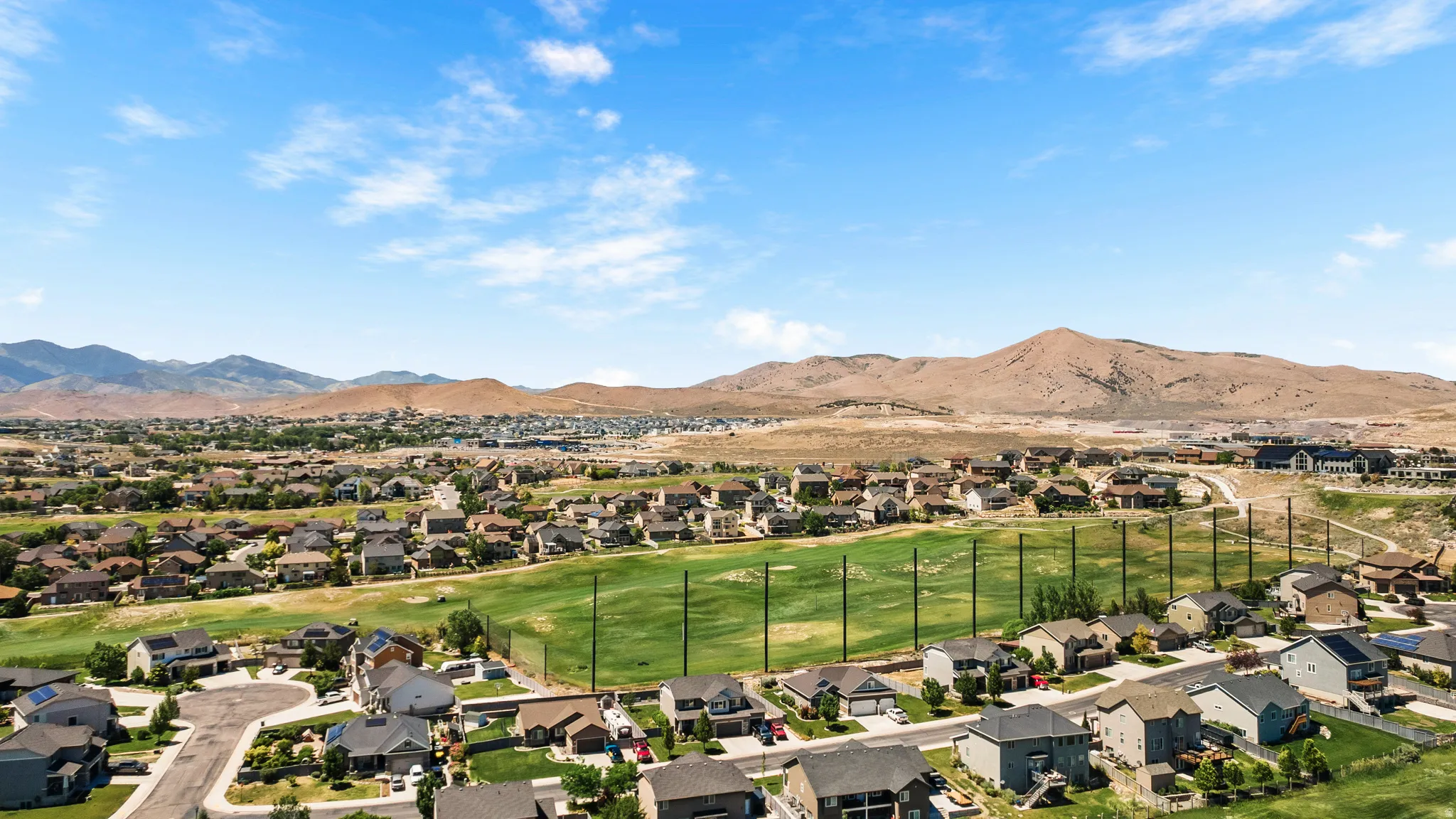 Aerial perspective showcasing a residential community with a manicured green space, surrounded by mountainous terrain