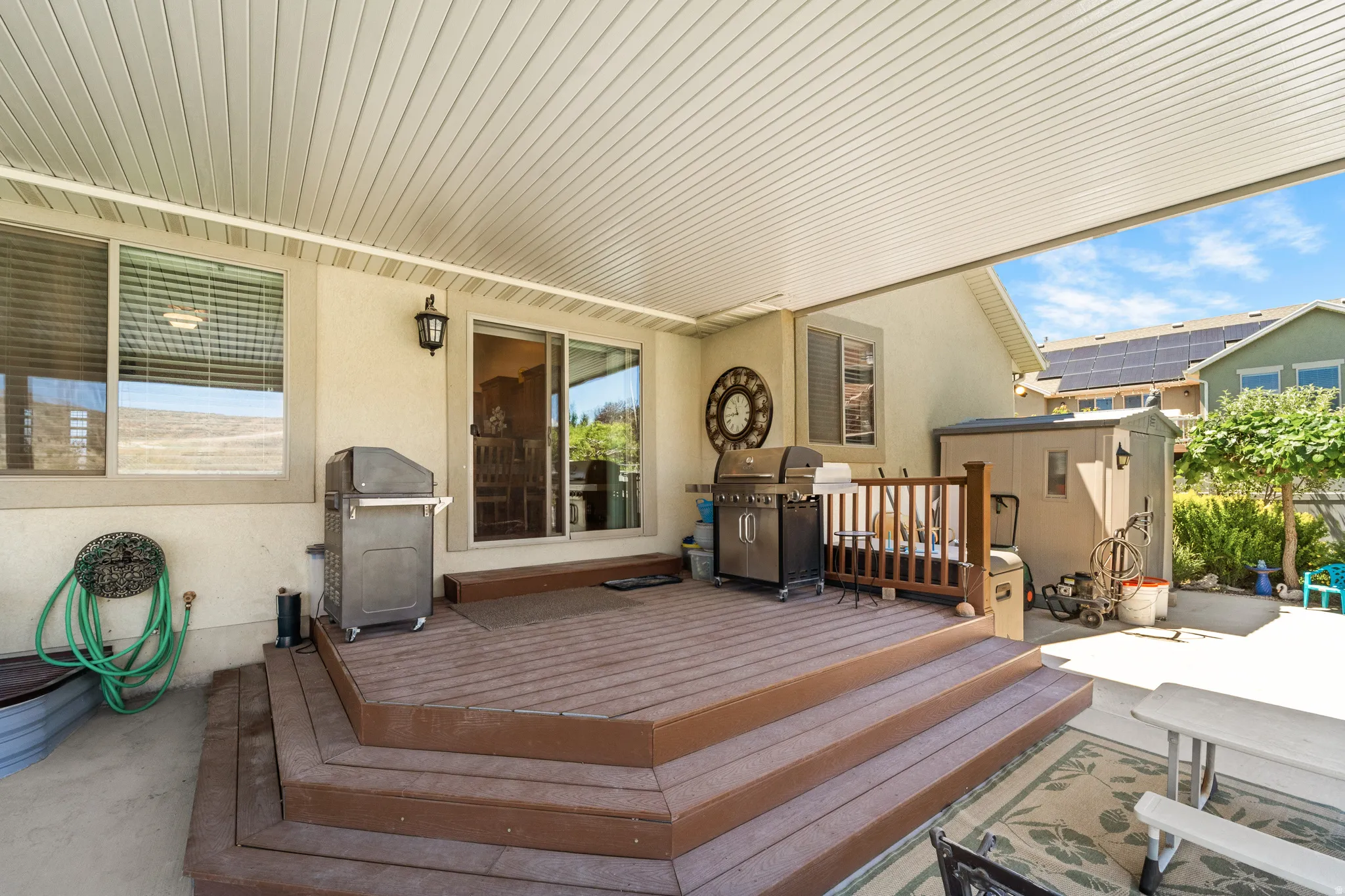 Covered patio with a multi-level composite deck, featuring a sliding glass door, exterior wall lighting, and a storage shed