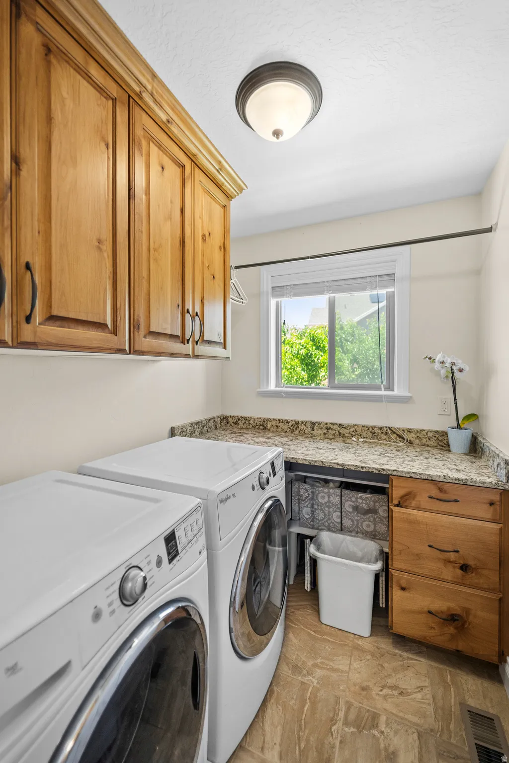 Laundry area featuring wood cabinetry, stone-look countertops, and tiled flooring