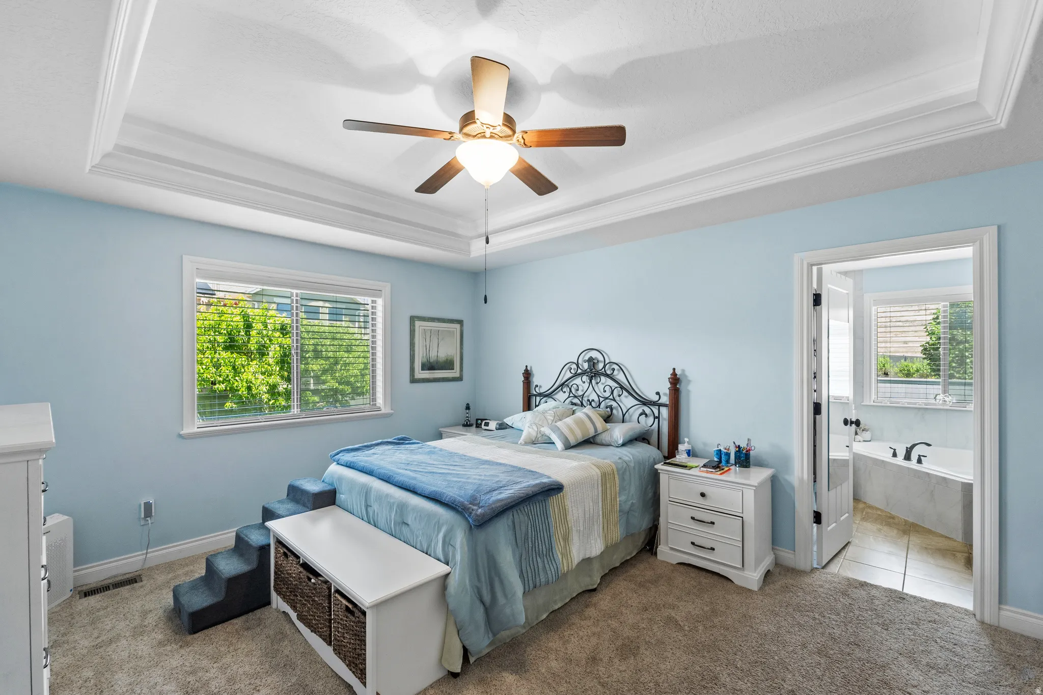 Recessed ceiling with layered crown molding, ceiling fan, and window featuring horizontal blinds