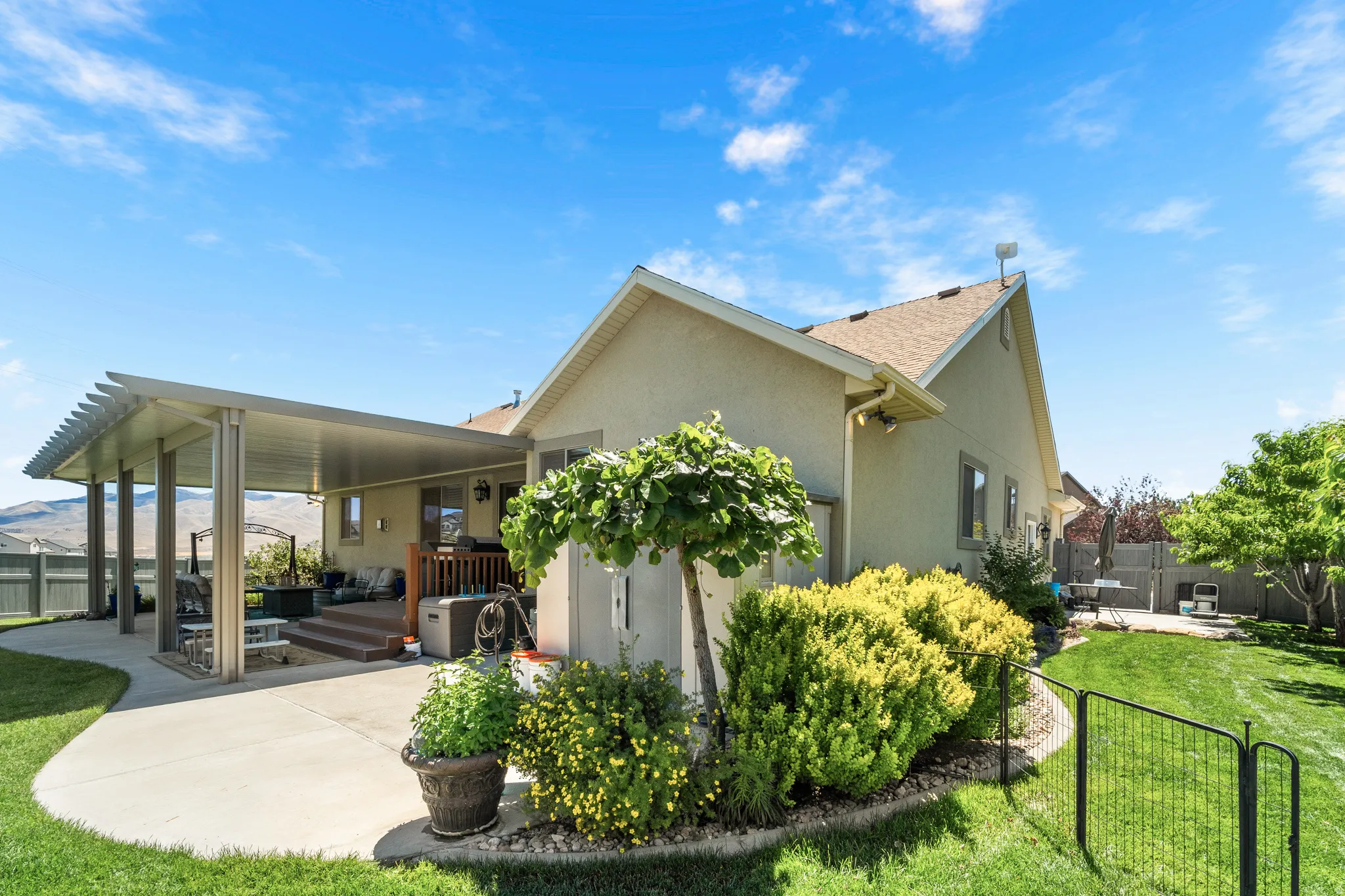 Rear exterior featuring a covered patio, concrete hardscaping, a multi-level deck, a fenced yard, and established landscaping