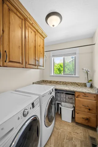 Laundry area featuring wood cabinetry, stone-look countertops, and tiled flooring