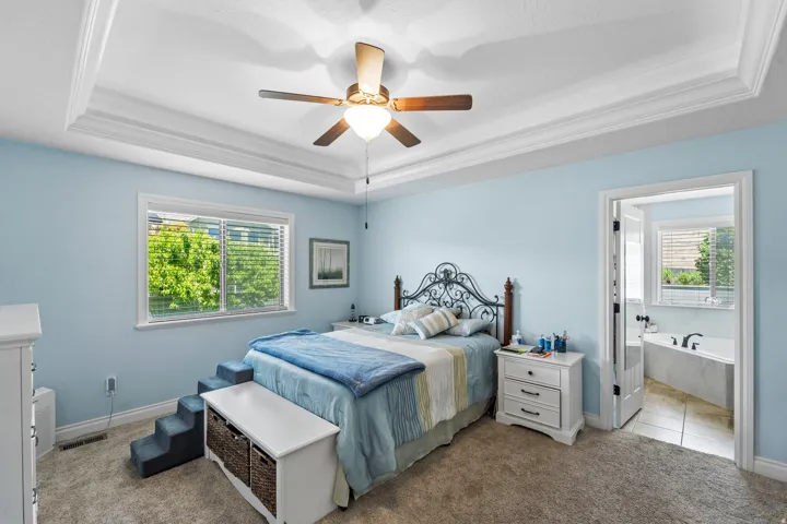 Recessed ceiling with layered crown molding, ceiling fan, and window featuring horizontal blinds