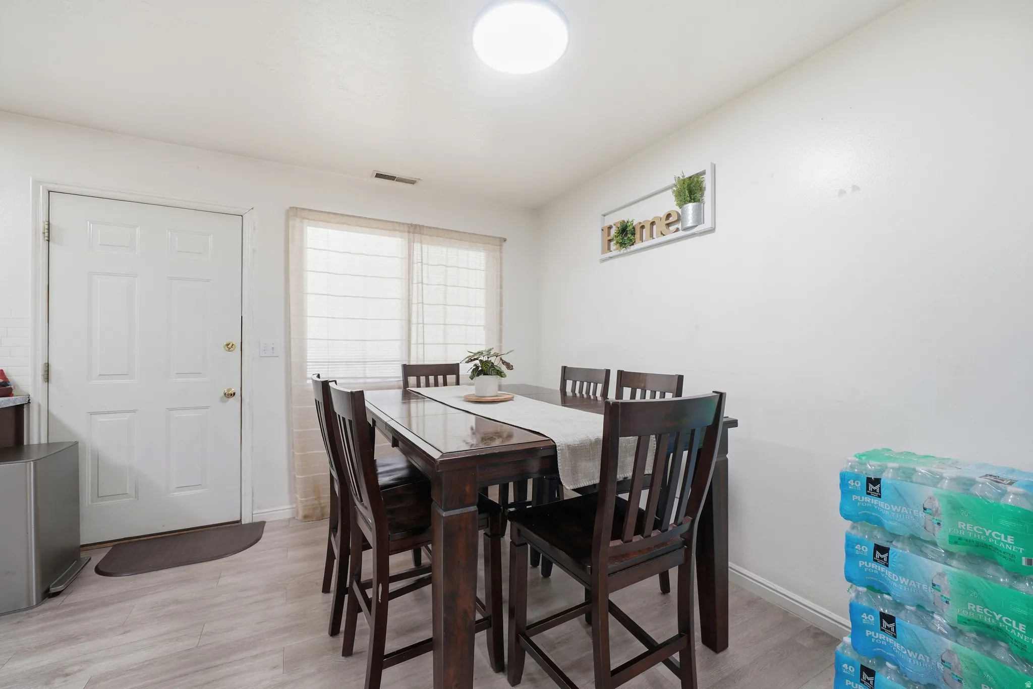 Dining area featuring light-toned wood-finish flooring, a white paneled door, and a window with blinds