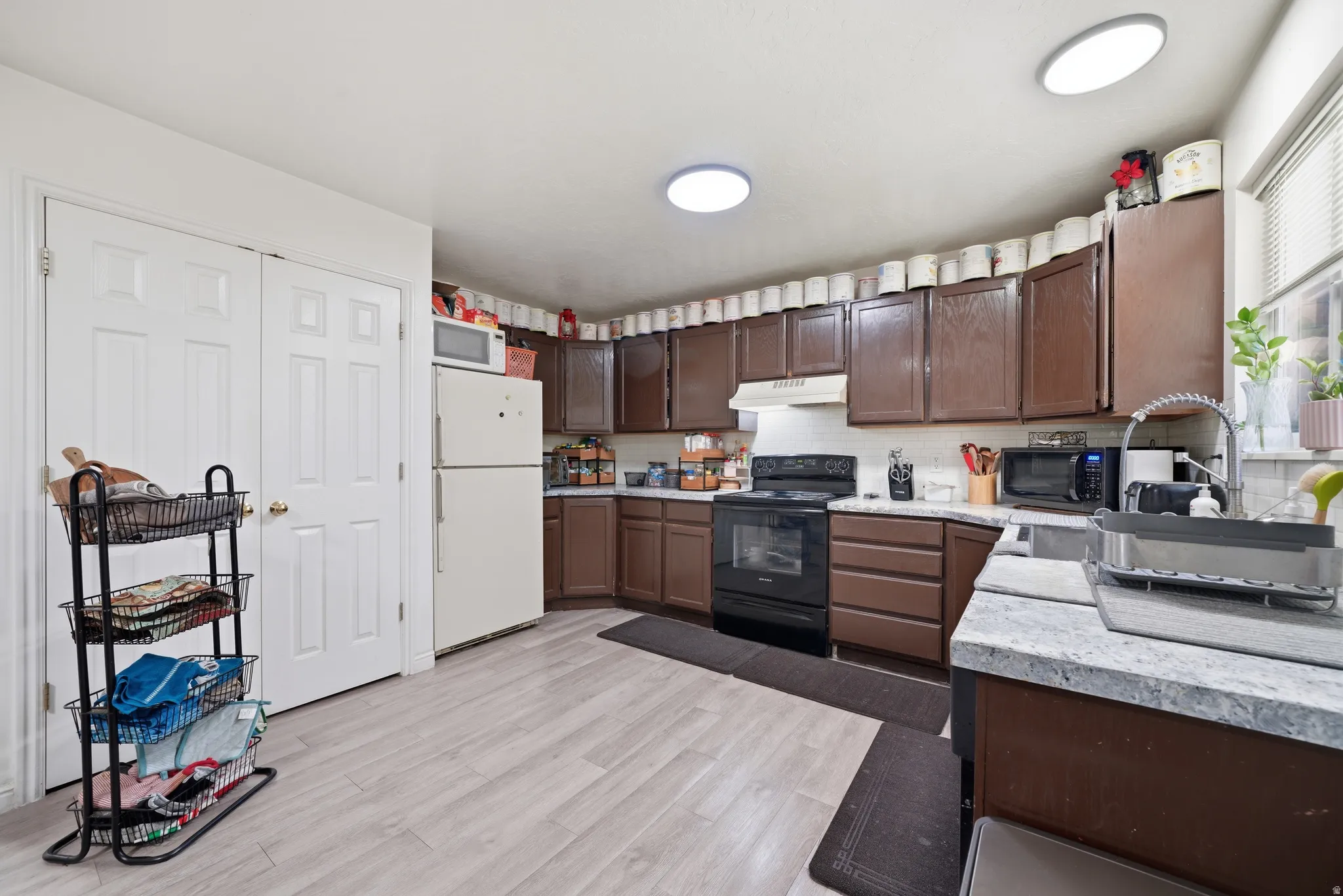 Kitchen featuring wood-finish flooring, dark wood cabinetry, light-toned countertops, and a white sink with a gooseneck faucet