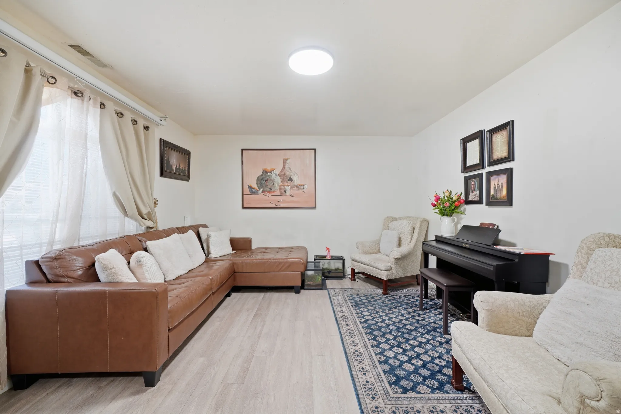 Spacious living area featuring light wood-finish flooring, a contemporary ceiling light fixture, and large window with blinds