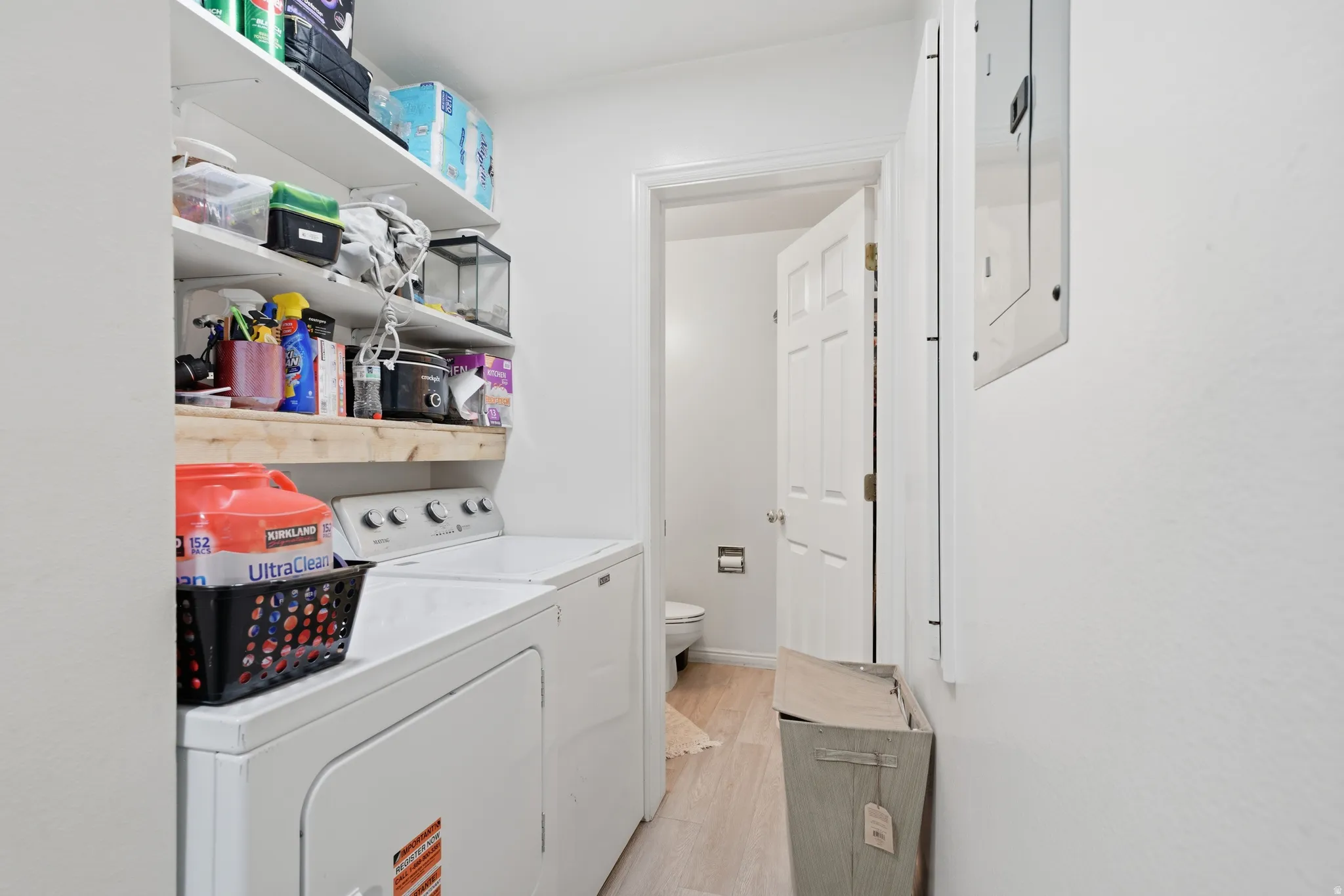 Dedicated laundry area featuring a white front-load washer and dryer, open shelving for storage, and light wood-finish flooring