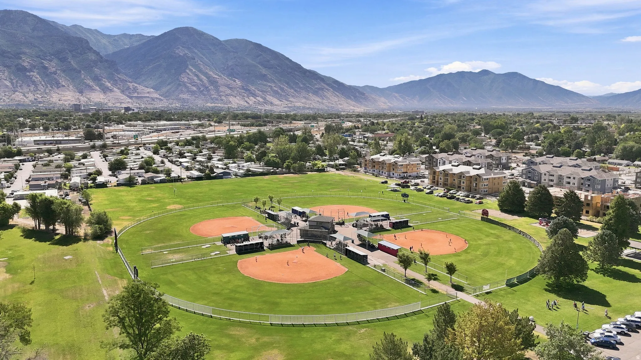 Expansive park grounds featuring multiple baseball fields, manicured green spaces, surrounding residential developments, and distant mountain backdrops