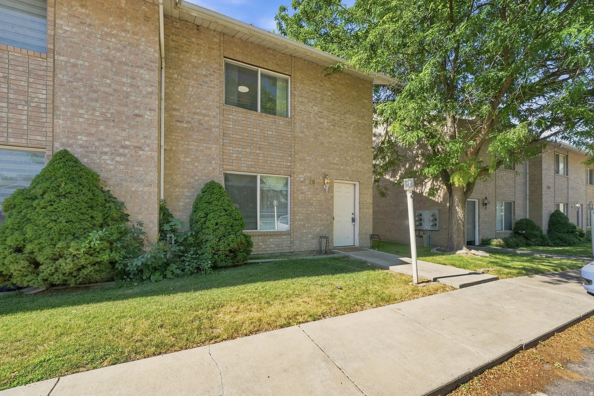 Two-story brick exterior featuring a white entry door, multiple windows, a concrete walkway, and established landscaping