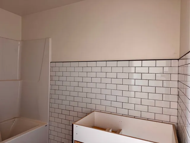White subway tile walls with dark grout, white tub, and white shower surround