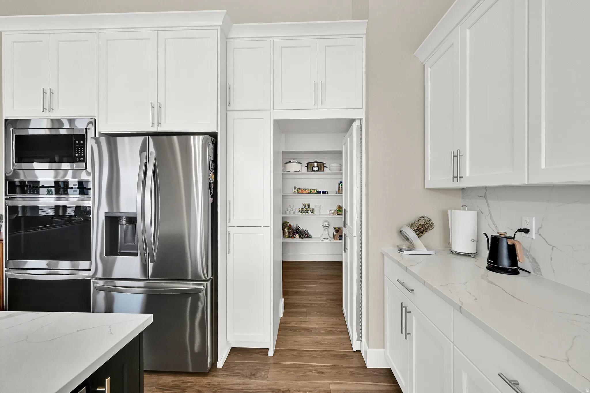 Kitchen featuring stainless steel appliances, white shaker cabinetry, light-toned countertops, and wood-finish flooring
