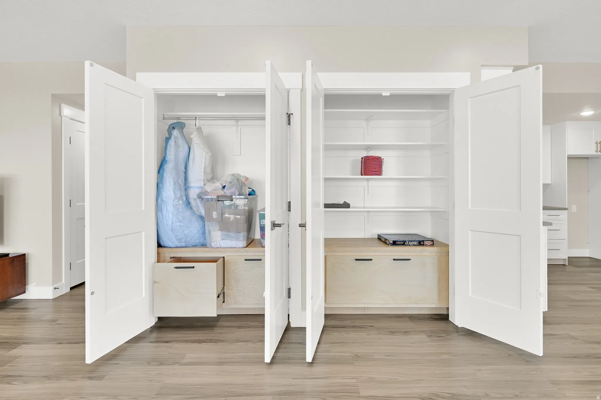 Built-in white storage closets featuring bi-fold doors, adjustable shelving, integrated wood-finish drawers, and hanging rods, all set against wood-finish flooring