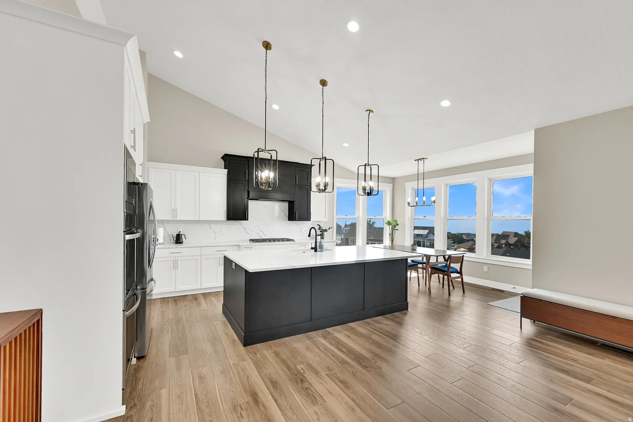 Spacious kitchen featuring an expansive island with a white countertop, two-tone cabinetry, wood-finish flooring, and a vaulted ceiling