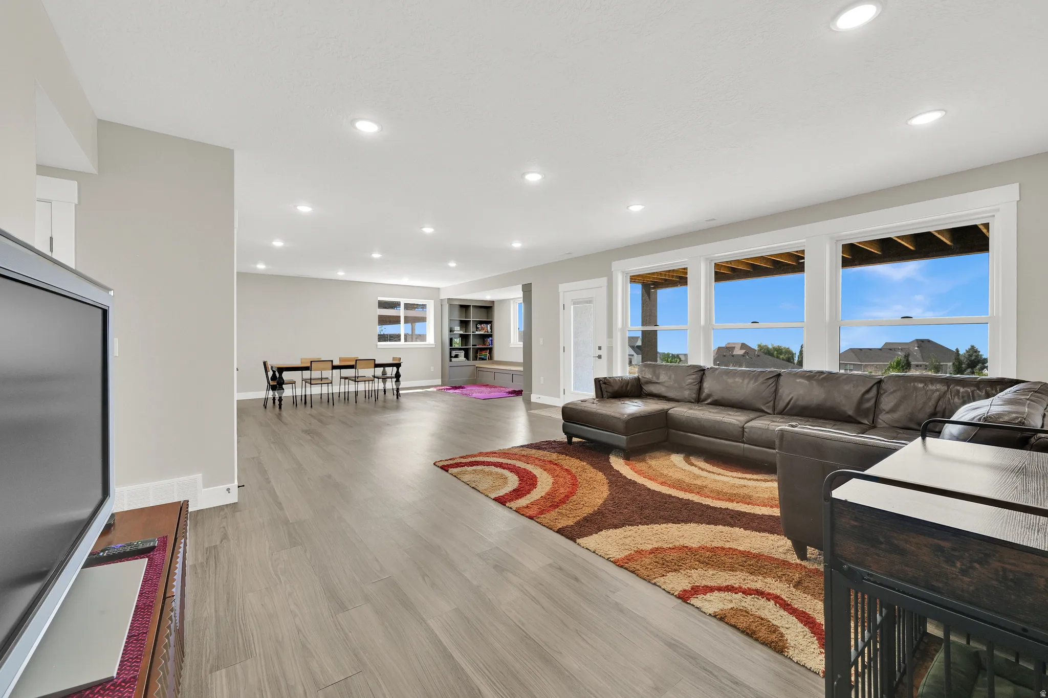 Spacious entertainment area featuring wood-finish flooring, recessed lighting, and large windows with white trim