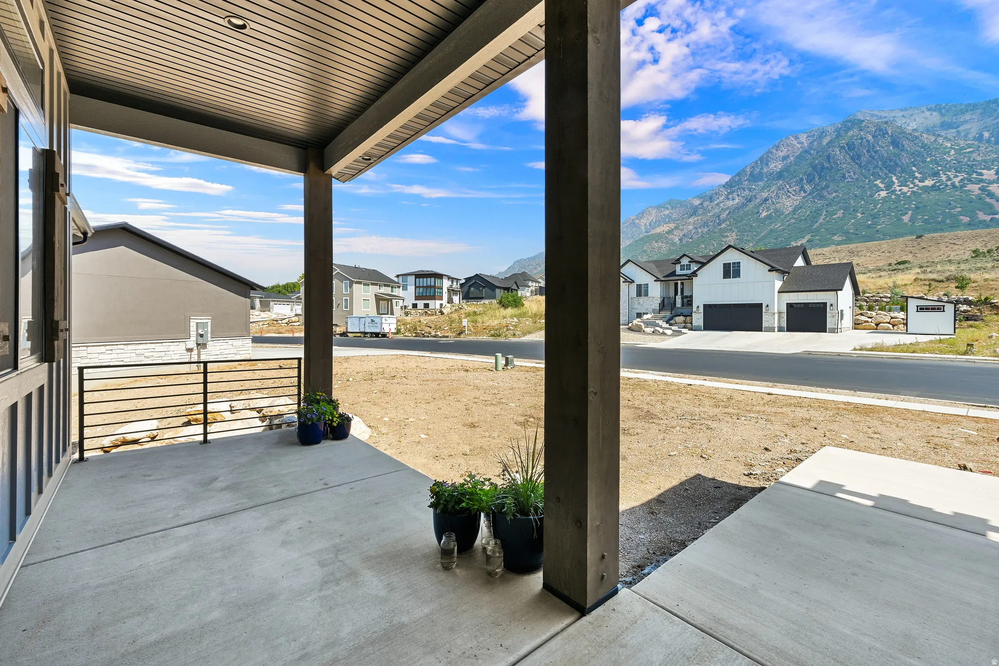 Covered concrete patio with horizontal metal railing, recessed lighting, and a wood-finish support beam
