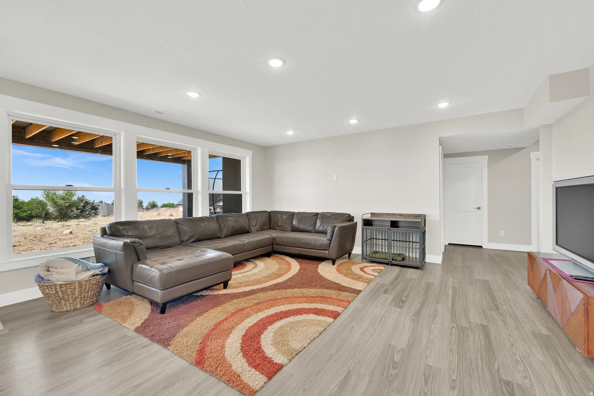 Spacious living area featuring light wood-finish flooring, recessed lighting, and a series of three large windows providing abundant natural light