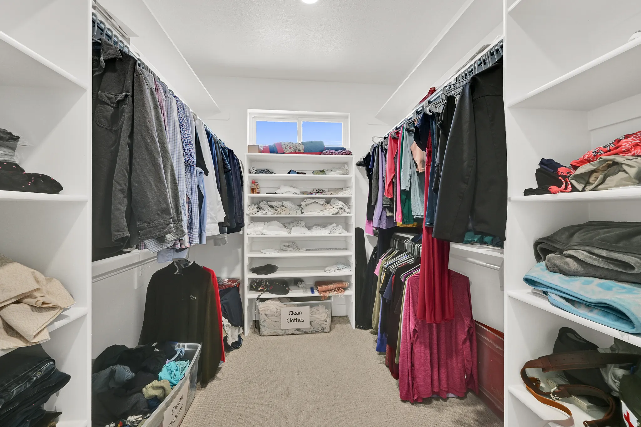 Walk-in closet featuring built-in white shelving, multiple hanging rods, recessed lighting, and a window for natural light