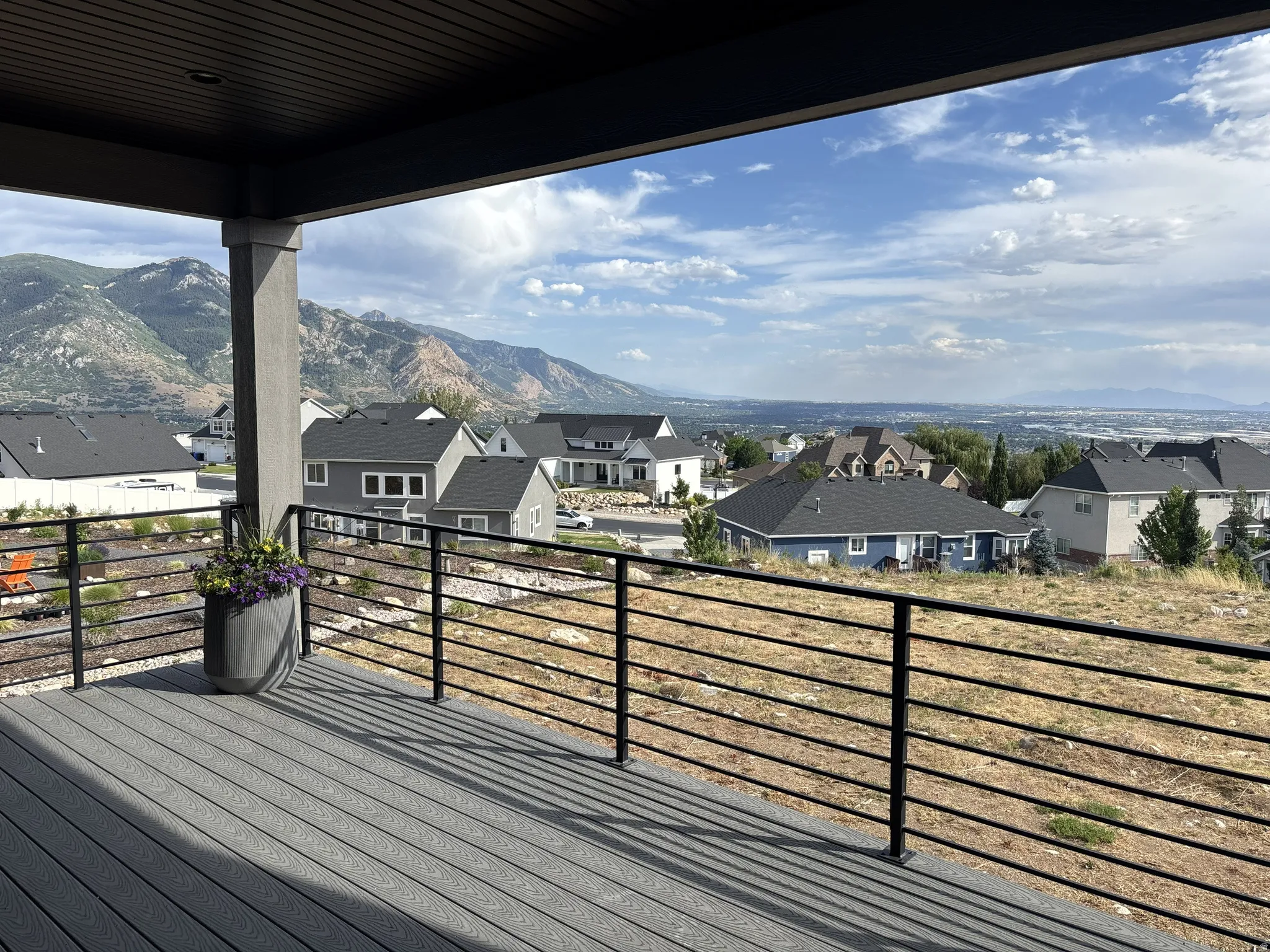 Spacious outdoor deck featuring composite decking, black metal railings, a covered patio area with a dark wood-finish ceiling, and expansive mountain scenery