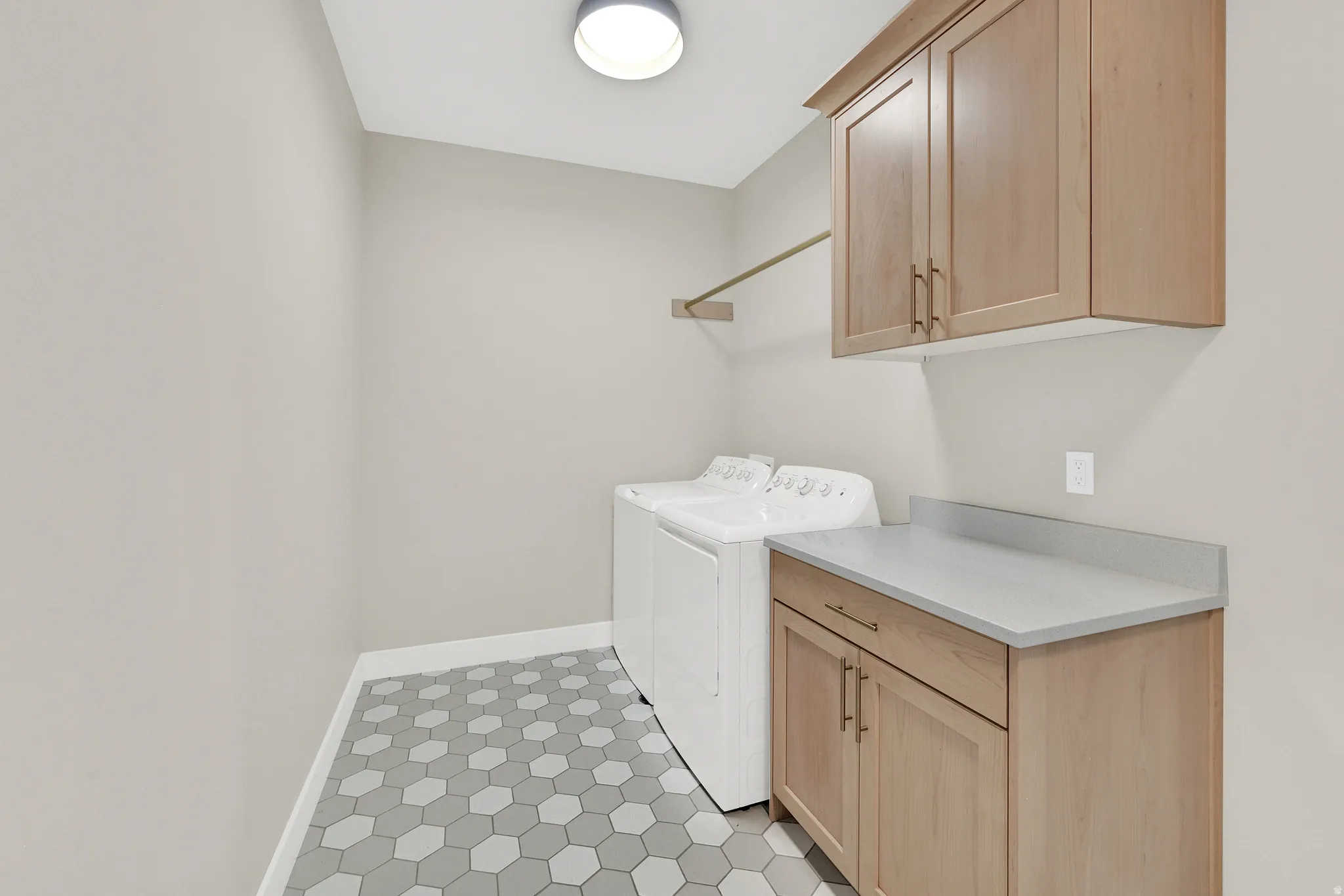 Laundry area with hexagon tile flooring, light wood-finish cabinetry, and a light-toned countertop