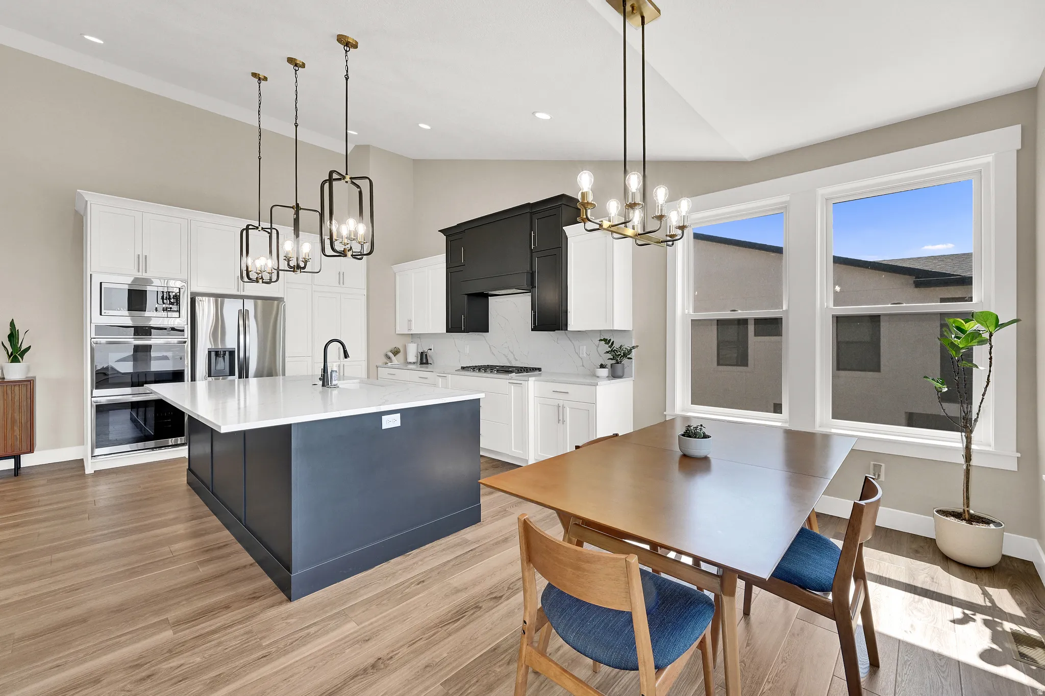 Open-concept kitchen and dining area featuring a prominent dark blue kitchen island with a white countertop, coordinating white upper and lower cabinetry, and a black range hood