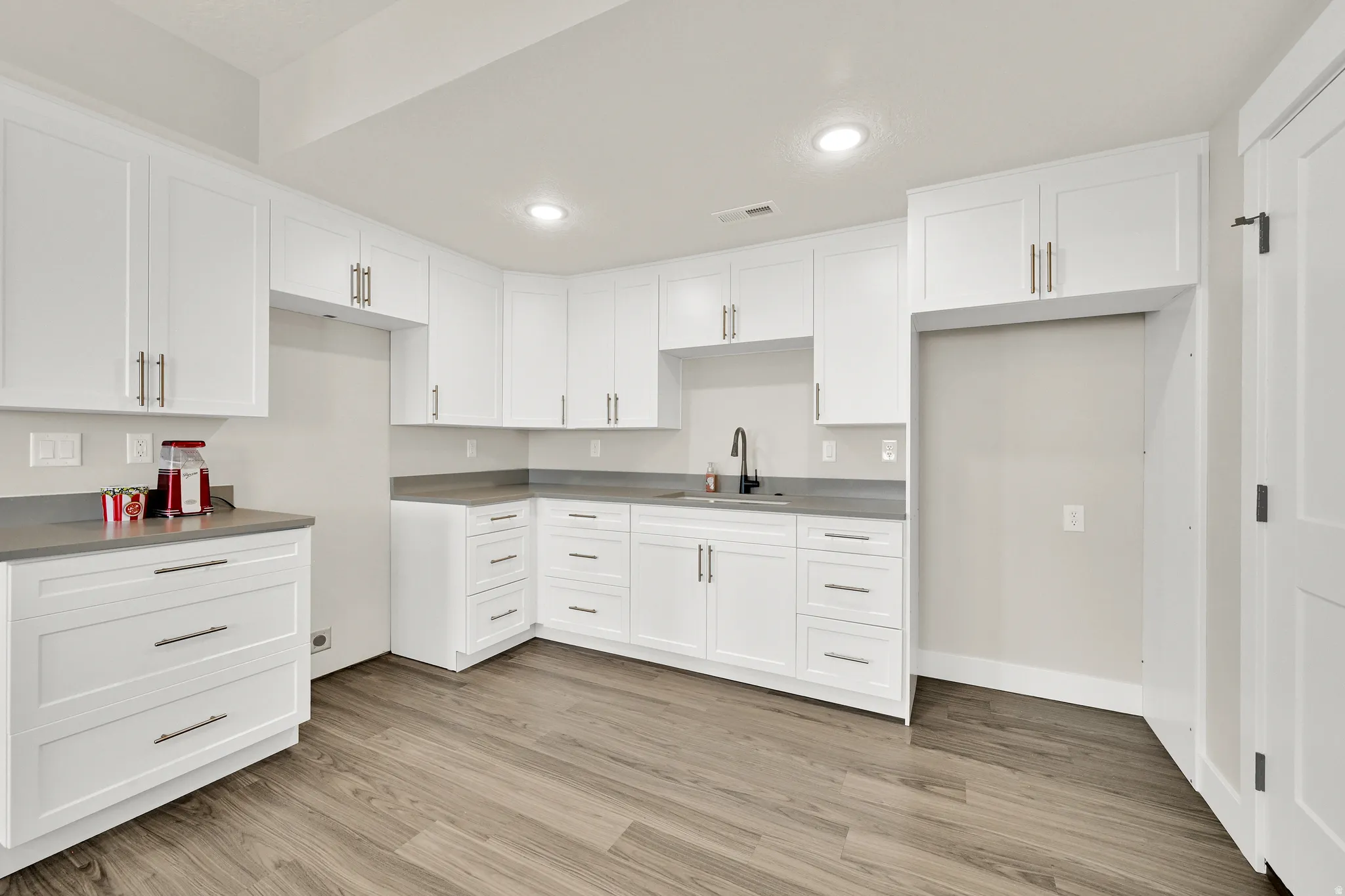 Kitchenette featuring white shaker-style cabinetry, dark wood-finish flooring, gray countertops, and a matte black gooseneck faucet