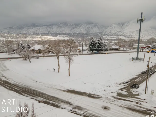 Expansive snow-covered lot featuring a paved road frontage and distant mountain scenery