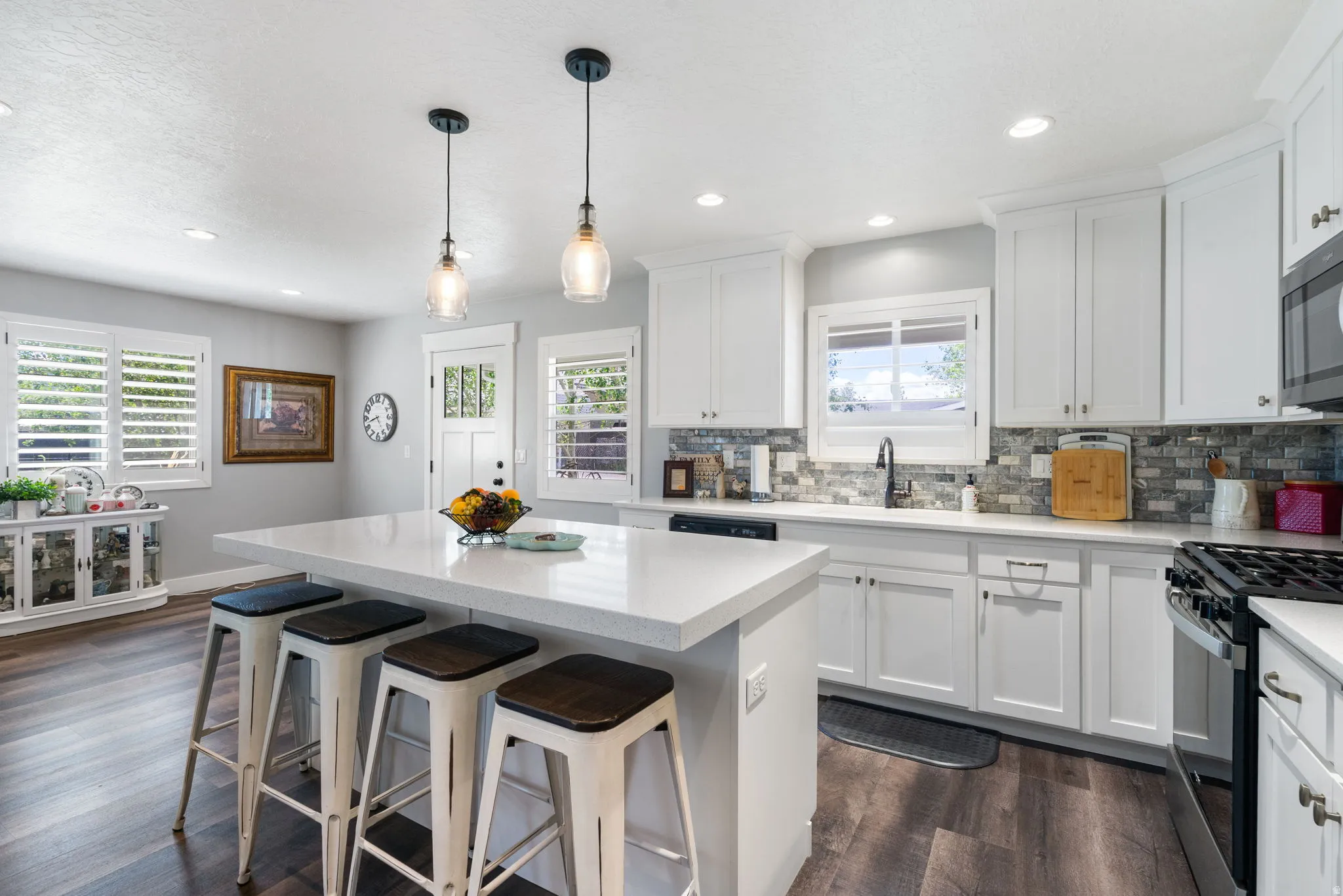 Bright kitchen featuring a central island with countertop seating, white cabinetry, integrated appliances, a mosaic tile backsplash, and wood-finish flooring