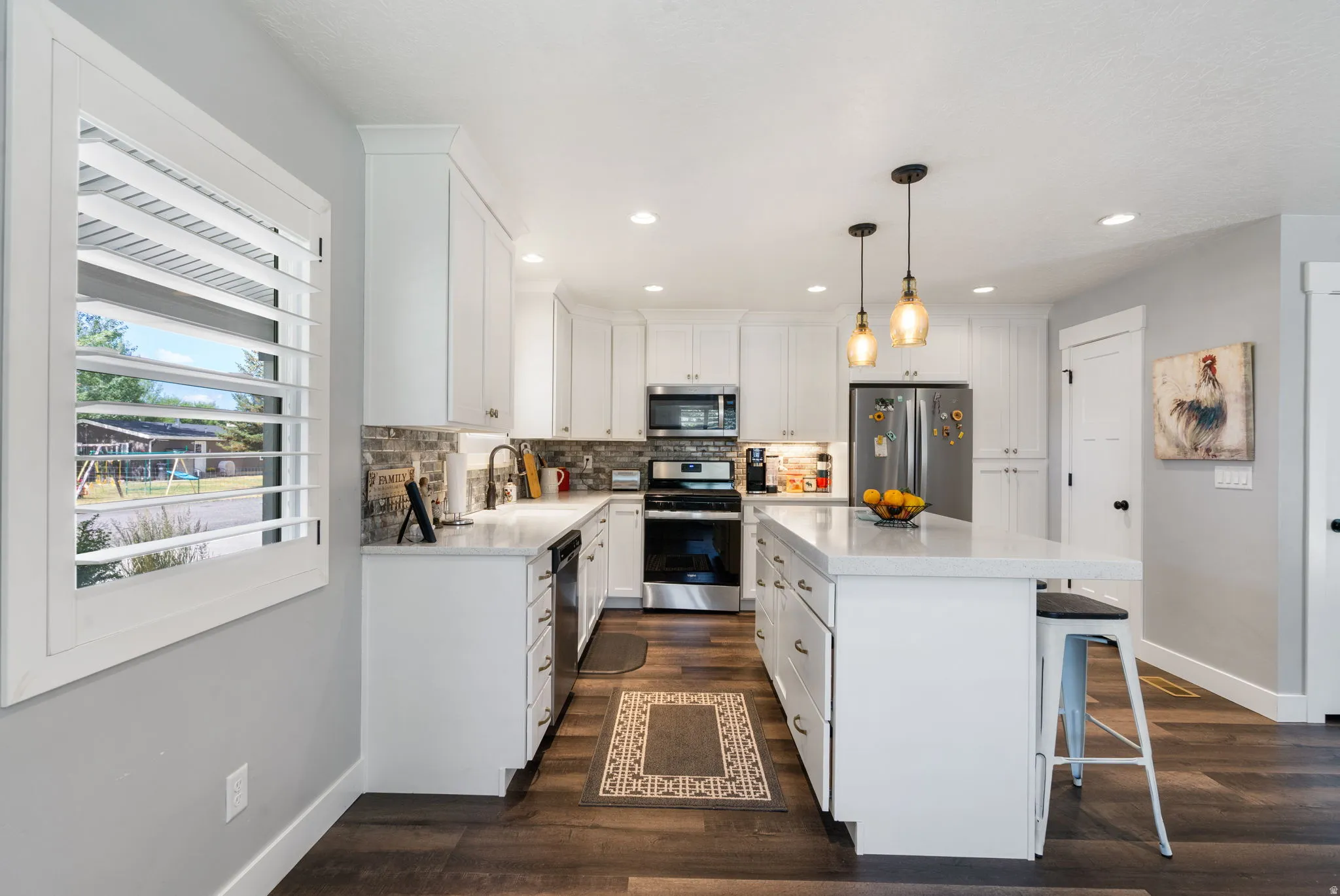 Spacious kitchen featuring an island with seating, pendant lighting, stainless steel appliances, and wood-finish flooring