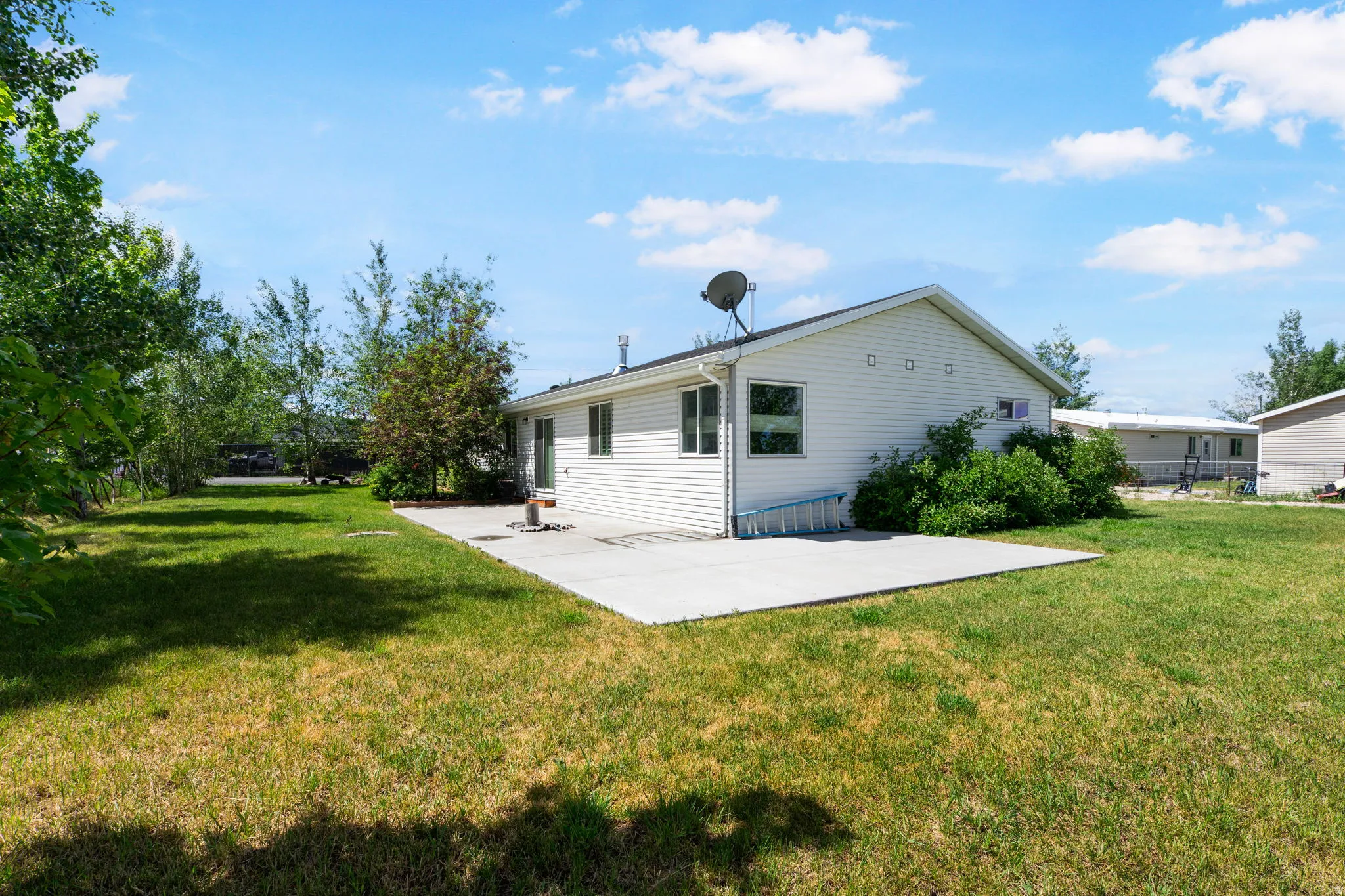 Spacious backyard featuring a large concrete patio, expansive lawn, mature trees, and white siding exterior