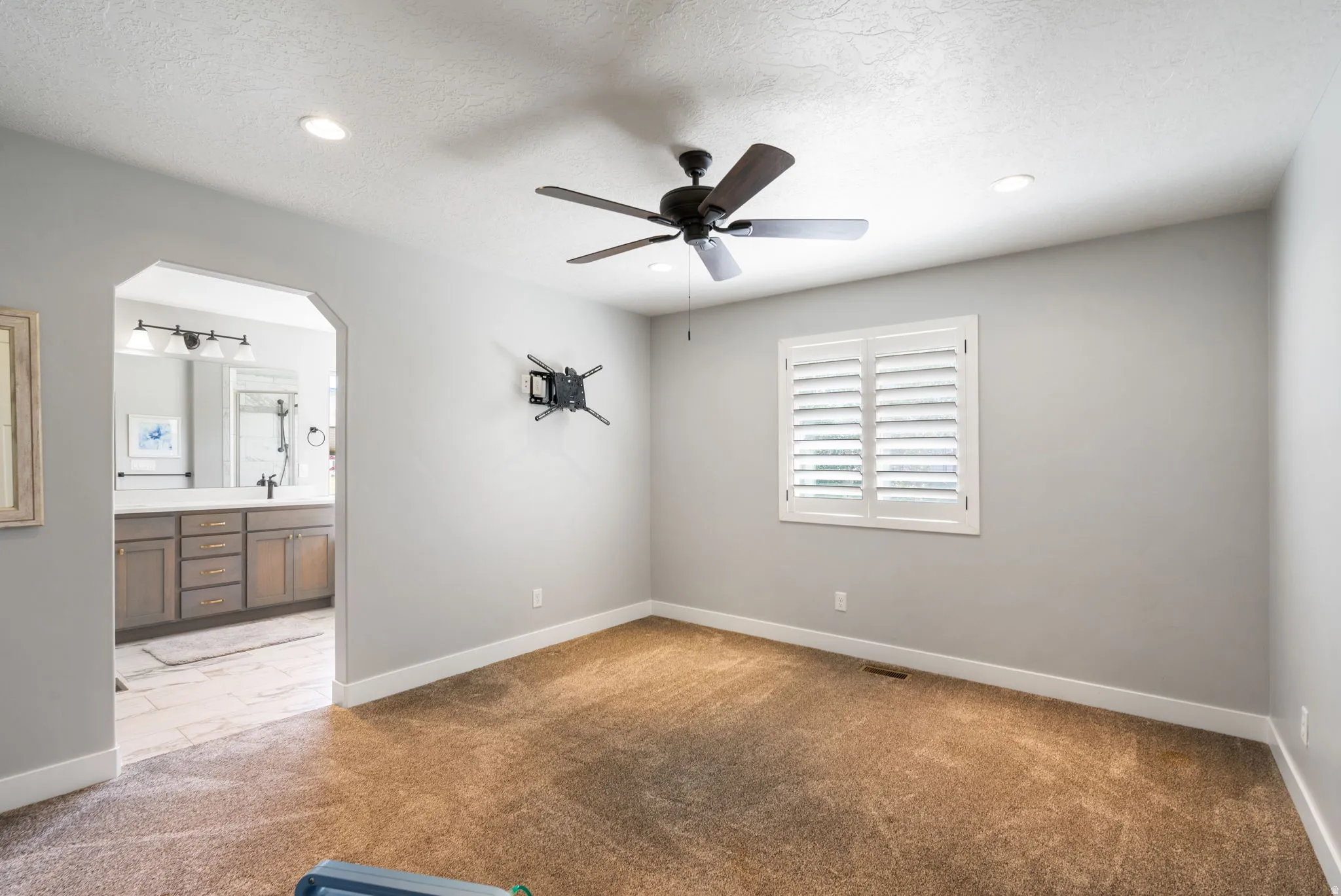 Carpeted bedroom featuring a ceiling fan with integrated lighting, recessed ceiling lights, and a window with white plantation shutters