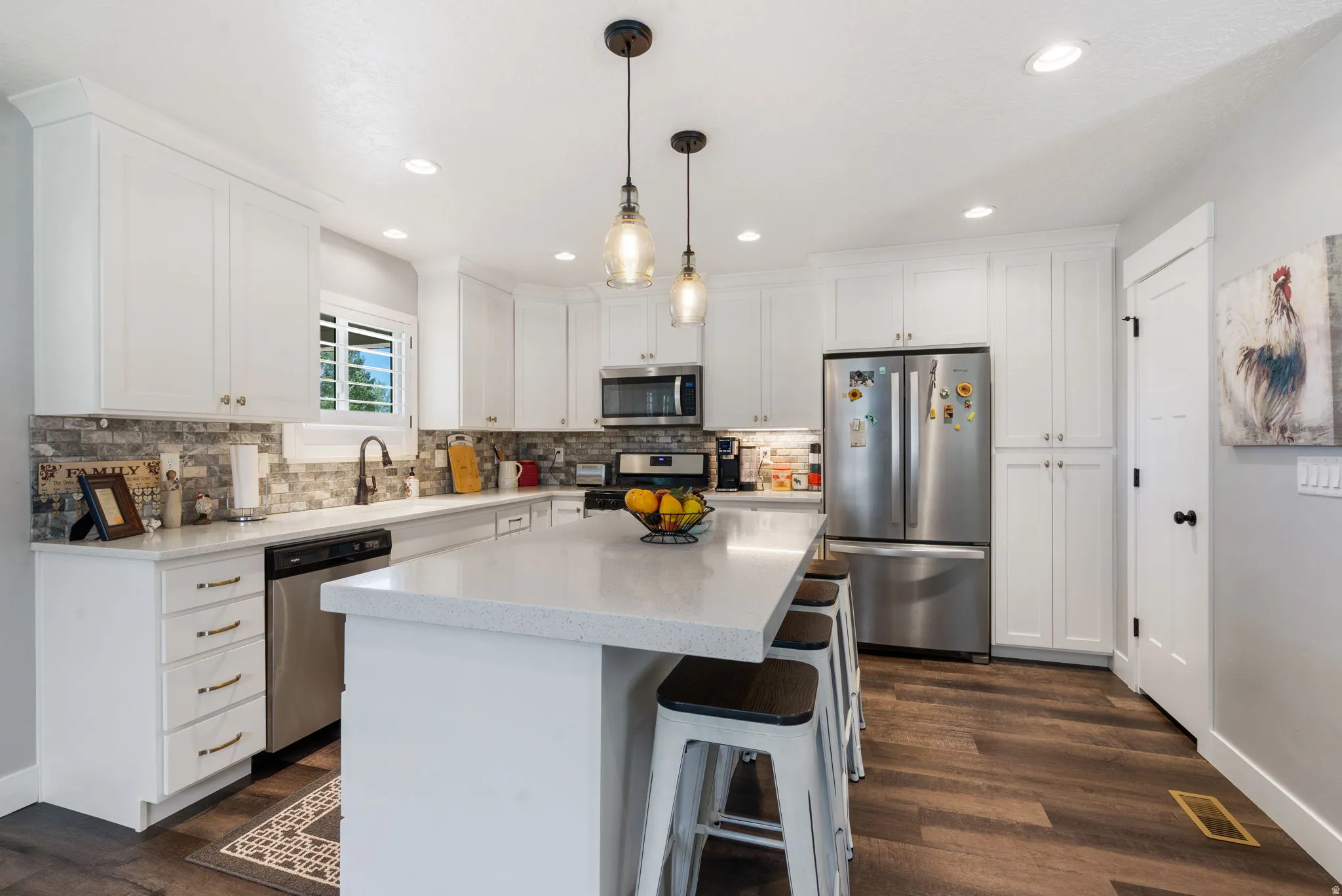 Spacious kitchen featuring an extended island with seating, white shaker cabinetry, stainless steel appliances, and wood-finish flooring