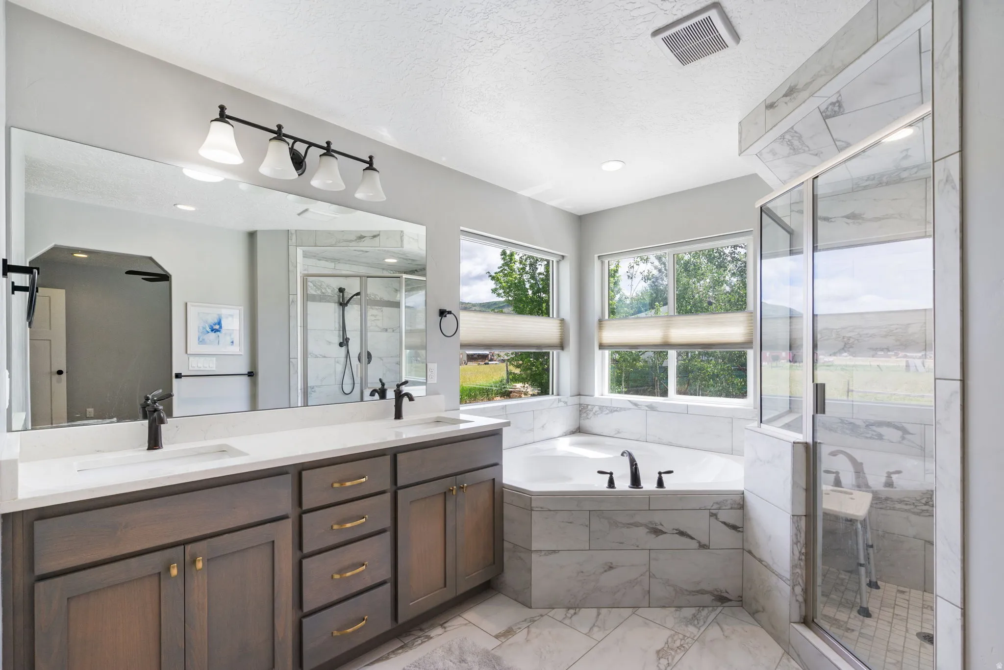 Spacious bathroom featuring a dual vanity with quartz countertops, a large soaking tub with marble-look tile surround, a walk-in shower with glass enclosure, and modern matte black fixtures