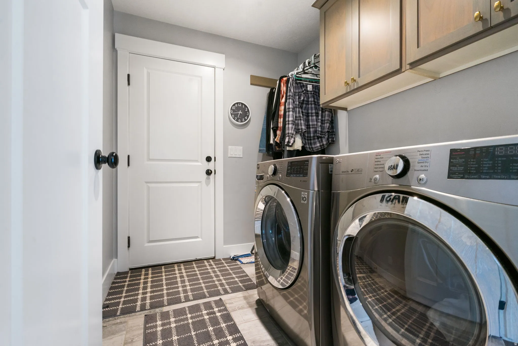 Dedicated laundry area featuring modern front-load appliances, upper cabinetry with brass hardware, and a built-in hanging rod