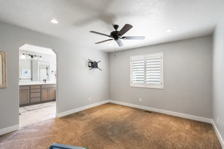 Carpeted bedroom featuring a ceiling fan with integrated lighting, recessed ceiling lights, and a window with white plantation shutters