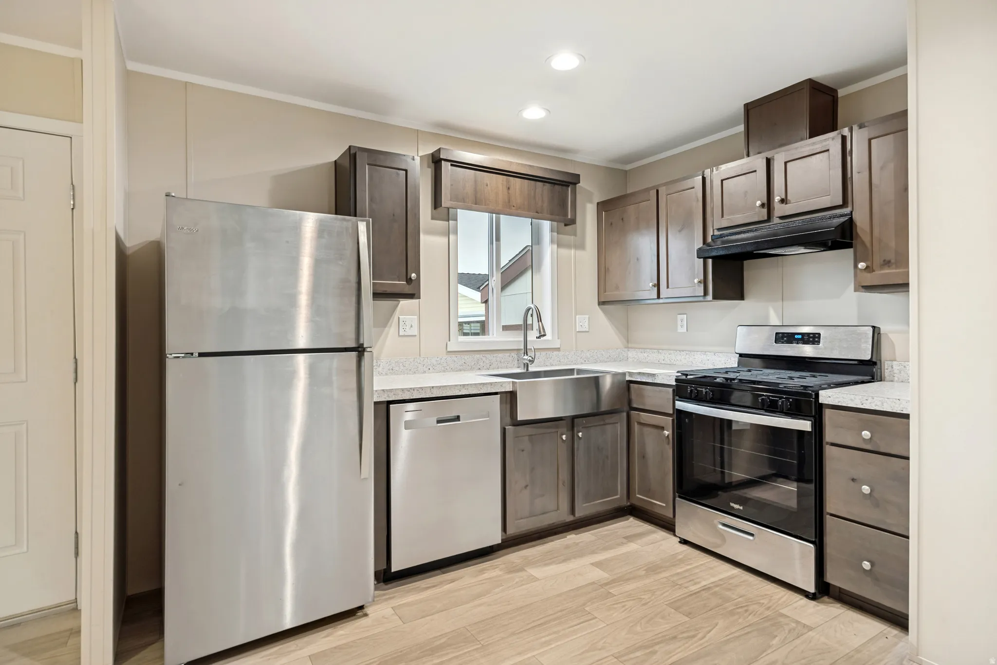 Kitchen featuring wood-finish flooring, stainless steel appliances, a farmhouse sink, light-toned countertops, and dark wood cabinetry