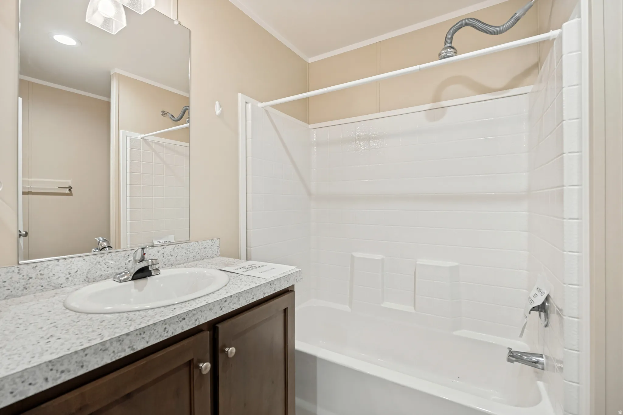 Bathroom featuring a white bathtub and shower combination, dark wood-finish vanity with a white speckled countertop, and an oval undermount sink with a chrome faucet