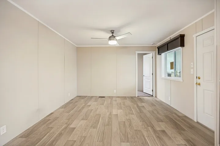 Spacious room featuring wood-finish flooring, a ceiling fan, and light-toned paneled walls