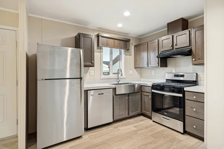 Kitchen featuring wood-finish flooring, stainless steel appliances, a farmhouse sink, light-toned countertops, and dark wood cabinetry