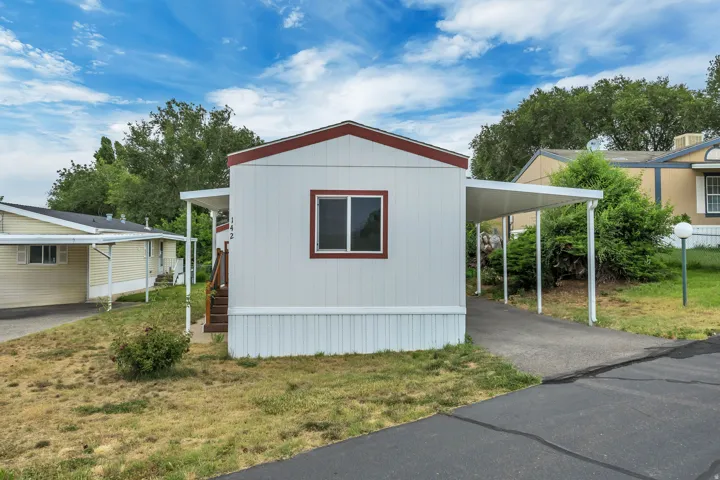 White exterior with red trim featuring a single window and an attached carport
